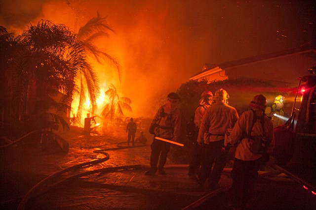 Tea Fire. Firefighters close to being overrun by flames from a home burring below them.