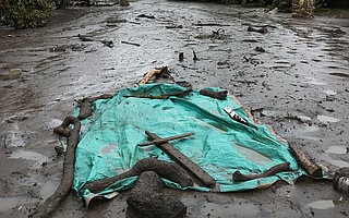 Neighbors placed a green tarp and cross over the remains of a woman killed by the flash floods.