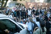 One student lividly holds his student ID up to the windshield of a Regent-filled van, while surrounding protestors prohibit driving and chant angrily.