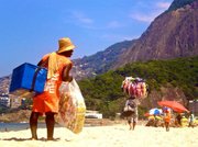 A vendor of the Carioca snack dream team - Matte Leão and Biscoitos Globos, looks for potential customers while a bikini vendor paces ahead of him.