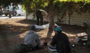 A Sheriff's deputy with the coroner's office examines the body of a deceased homeless man in Pershing Park as his companions sit nearby