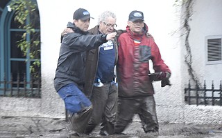 Jason Copus (left) and Mark Olson help Steve Wrolstae through thick mud on Coast Village Road (Jan. 9, 2018).